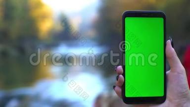 大自然中的智能手机4k技术概念：带绿色屏幕的手机，在瀑布上跟踪哑光